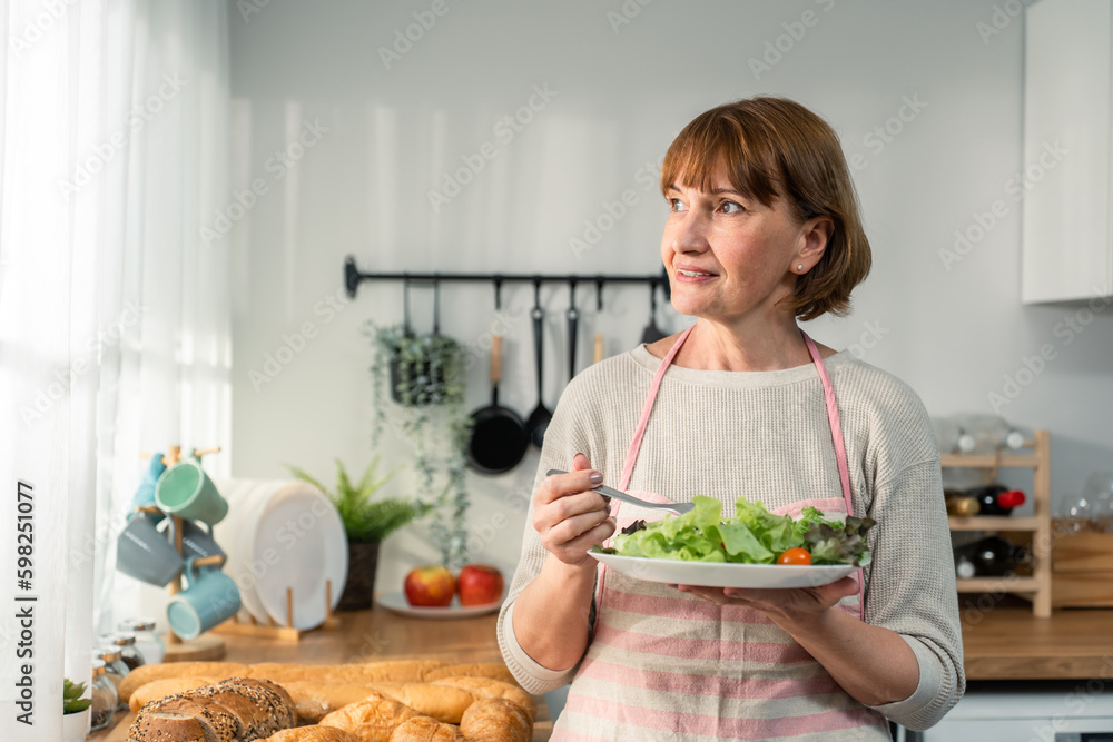 Caucasian senior woman eatting a bowl of vegetables on hands in house. 