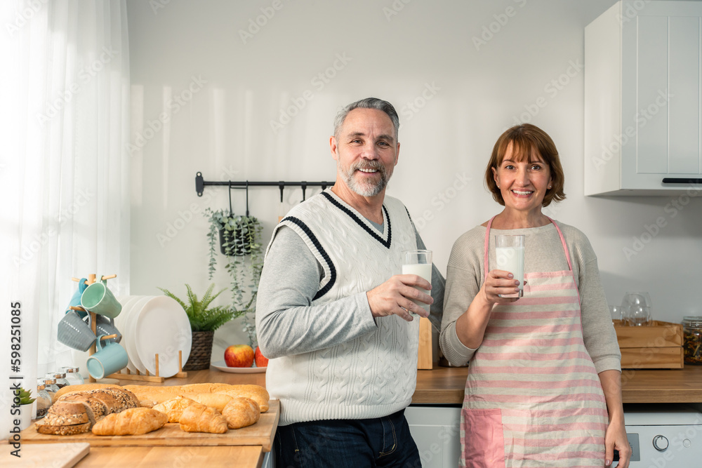 Caucasian senior mature couple drink a glass of milk in kitchen at home. 