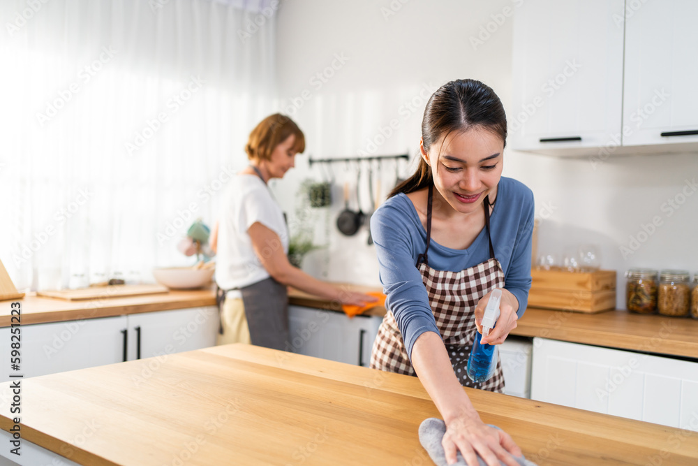 Caucasian senior elderly woman cleaning kitchen in house with daughter. 