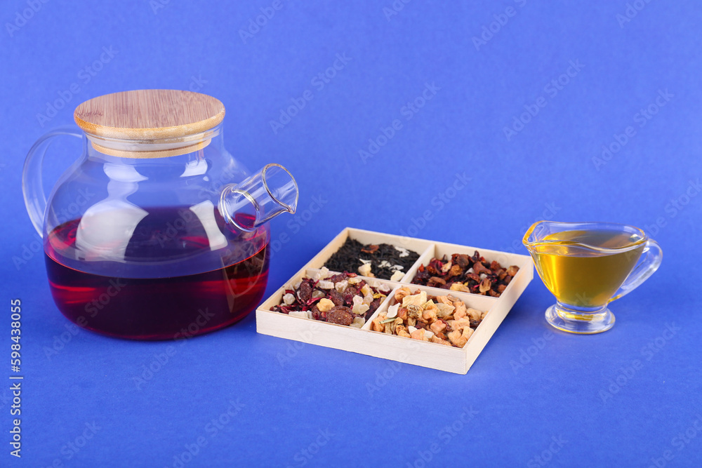 Teapot, honey and box with different dried fruit tea on blue background