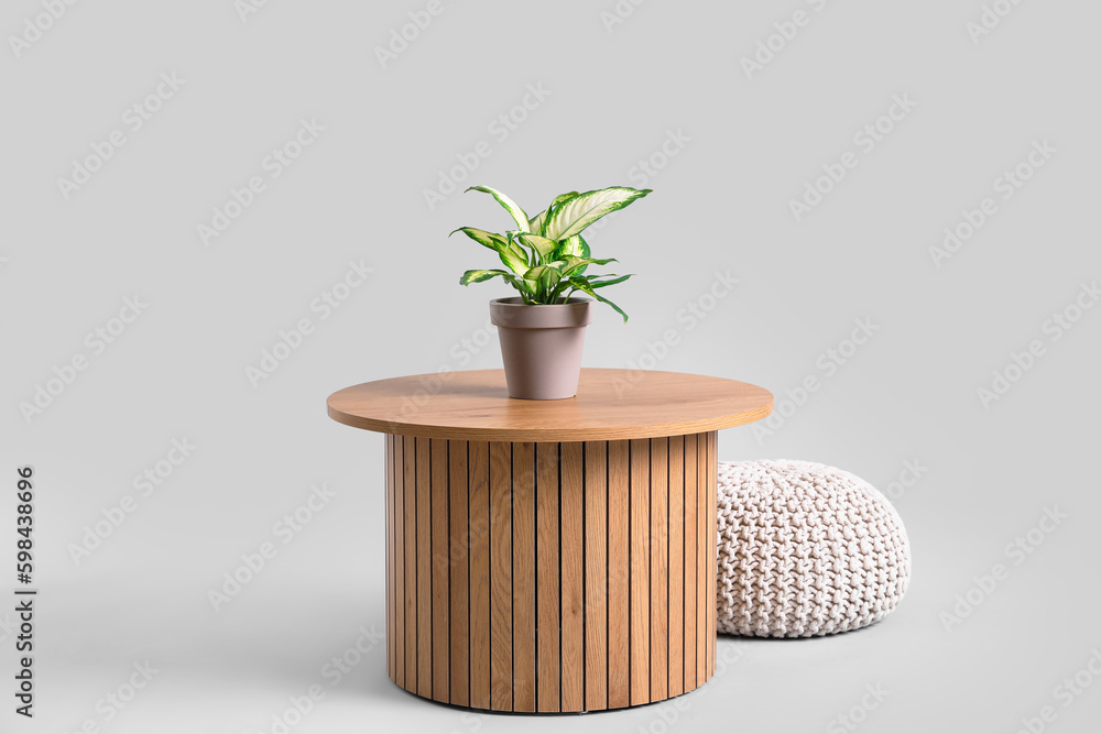 Wooden coffee table with houseplant and pouf on grey background