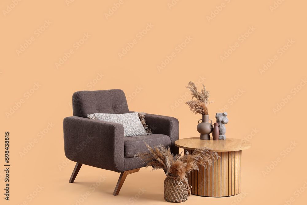 Wooden coffee table with pampas grass in vase and woman figurine near armchair on beige background