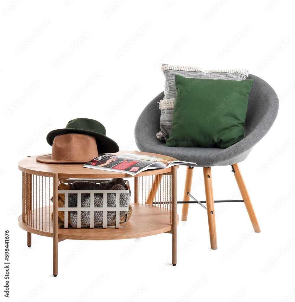 Coffee table with magazine and hats near cozy armchair isolated on white background