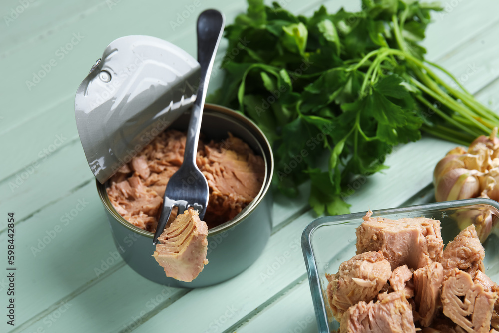 Opened tin can and bowl with delicious tuna on green wooden table, closeup