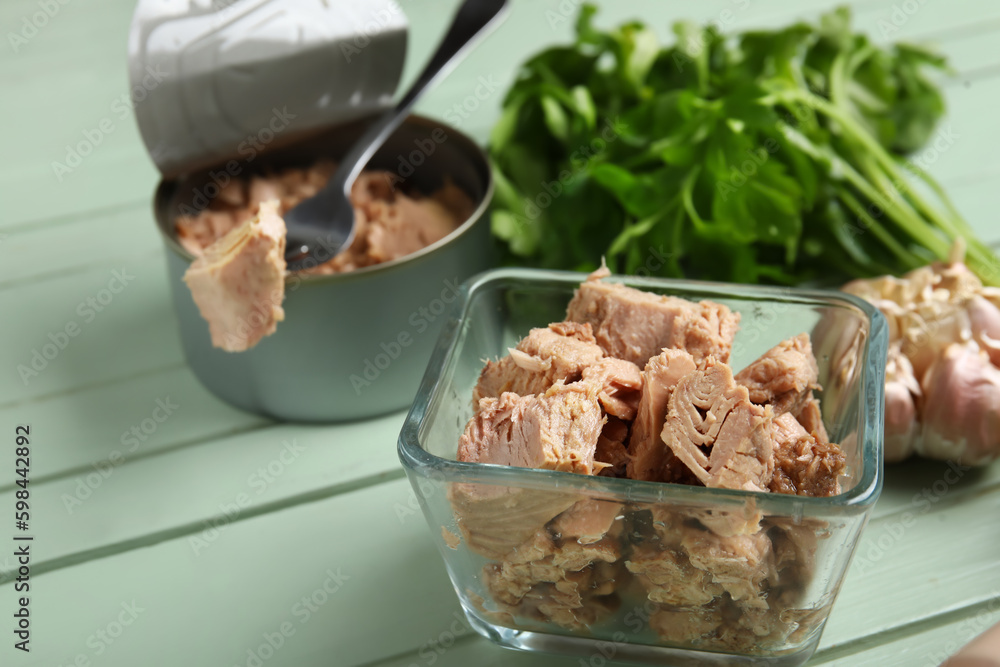 Opened tin can and bowl with delicious tuna on green wooden table, closeup