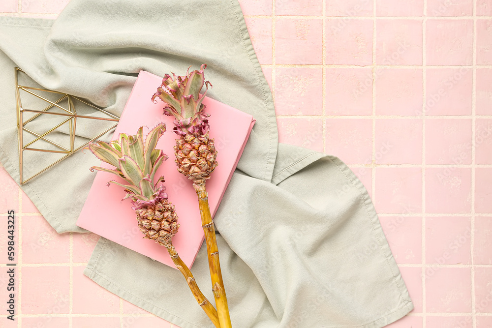 Decorative pineapples with book and napkin on pink tile background