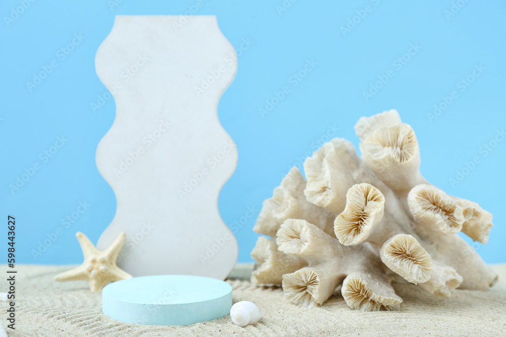 Decorative plaster podiums, coral, starfish and seashells in sand on blue background