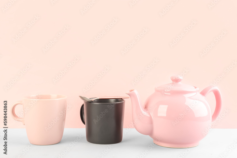 Teapot, mugs and spoon on pink background