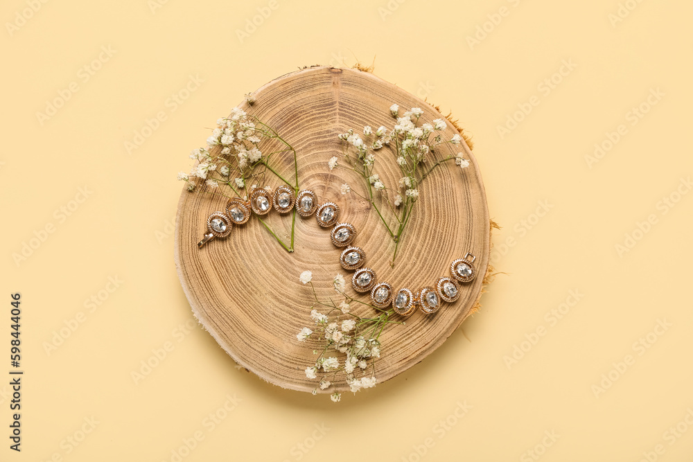 Wooden stand with golden bracelet and flowers on yellow background