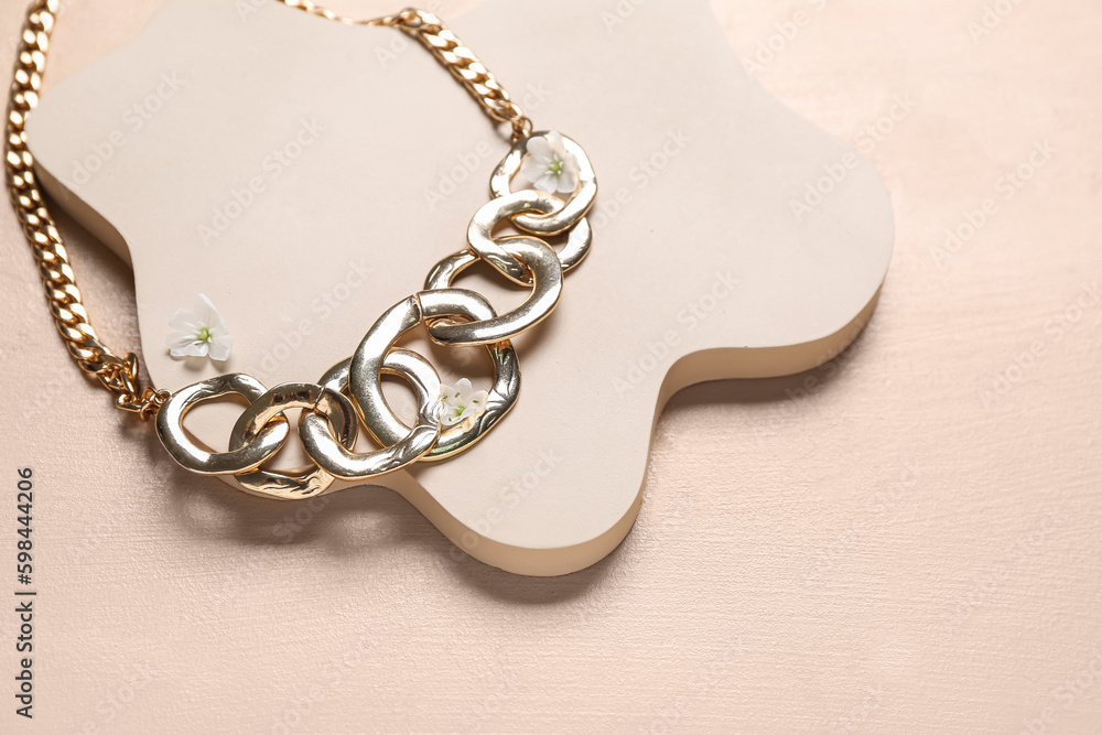 Showcase pedestal with golden necklace and flowers on beige background, closeup