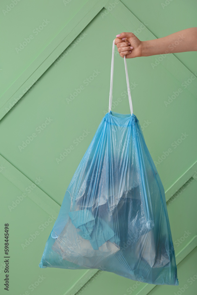 Female hand holding full garbage bag on green background