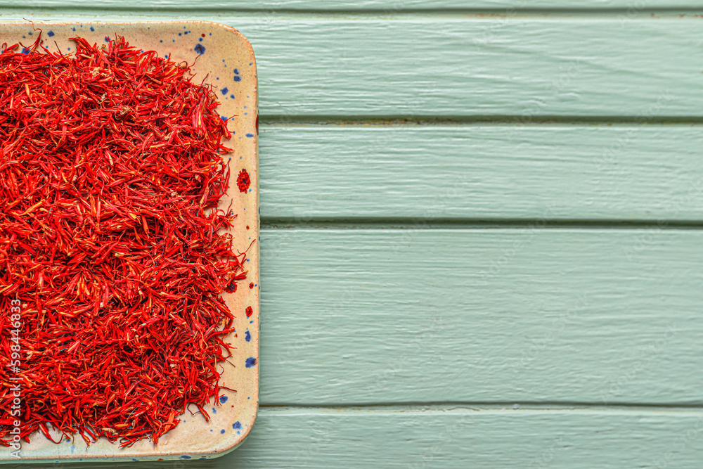 Plate with pile of saffron on blue wooden background