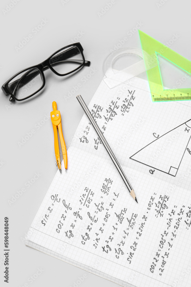 Copybook with maths formulas, glasses and stationery on grey background