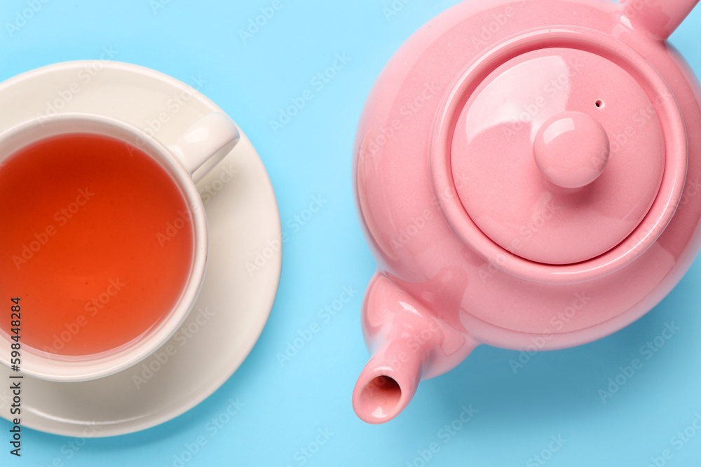 Ceramic teapot with cup of tea on blue background