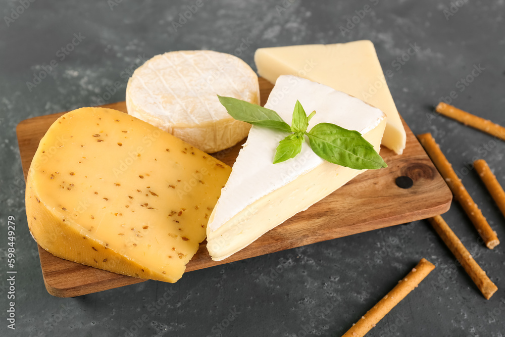 Wooden board with different types of cheese on green background