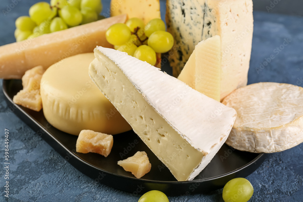 Plate with different types of cheese on blue background