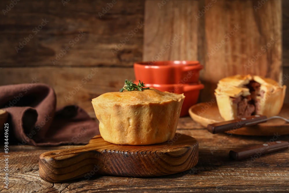 Board with tasty meat pot pie on wooden background