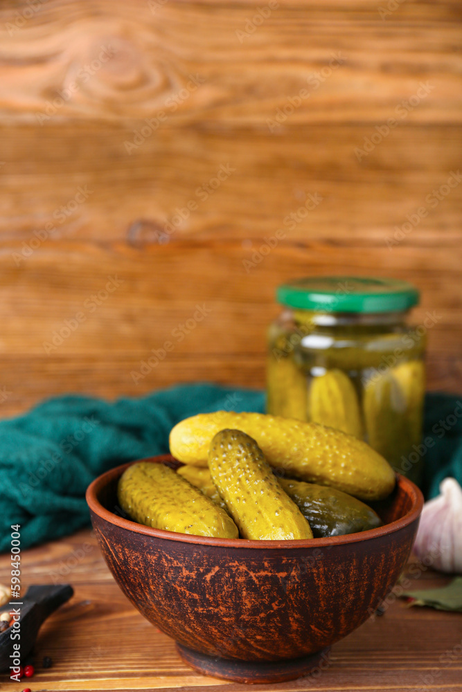 Jar and bowl with tasty canned cucumbers on wooden table