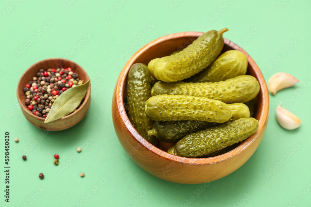 Bowl of tasty canned cucumbers with ingredients on pale green background