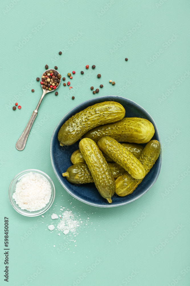 Bowl of tasty canned cucumbers with spices on blue background