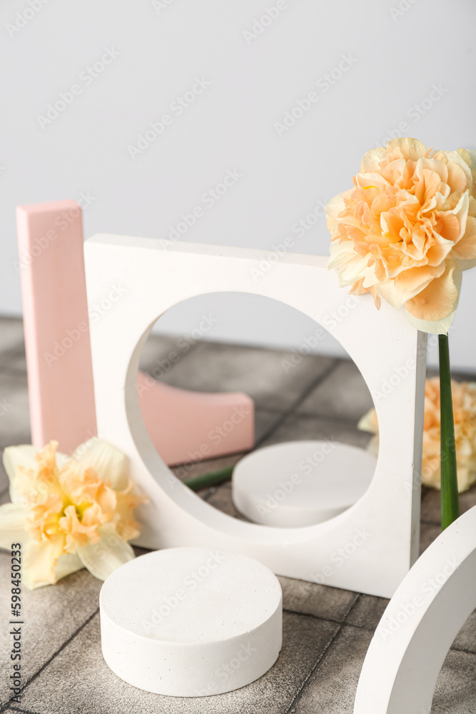 Decorative plaster podiums with daffodils on tile against grey wall