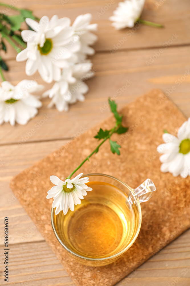 Glass cup of tea with chrysanthemums on wooden table