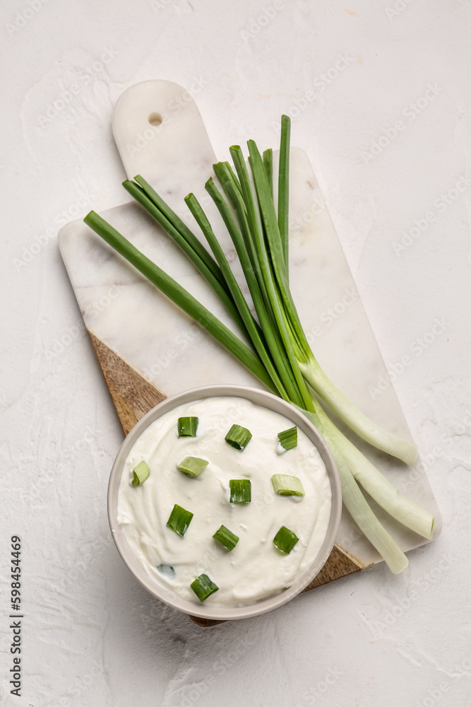 Bowl of tasty sour cream with green onion on light background