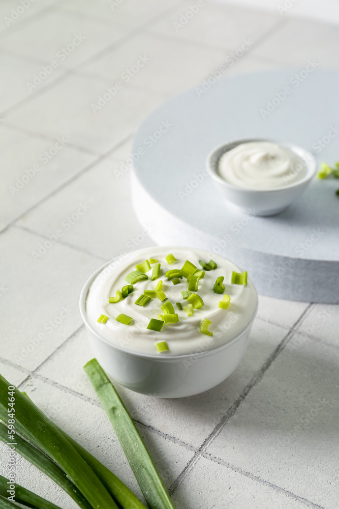 Bowl with sour cream and sliced green onion on white tile table