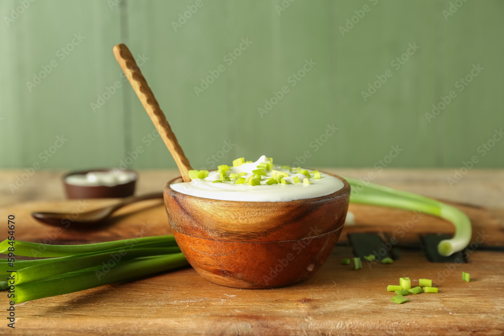 Bowl with sour cream and sliced green onion on brown wooden table near green wall