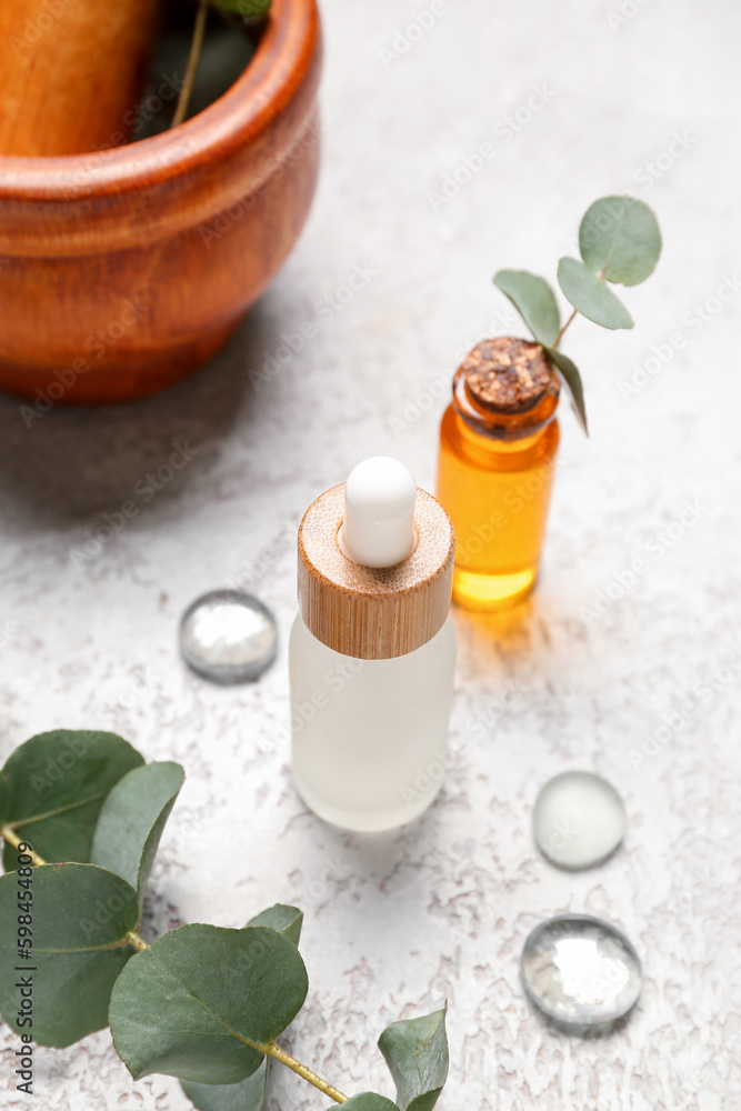 Cosmetic oil bottles with wooden mortar and pestle and eucalyptus branch on grey textured background