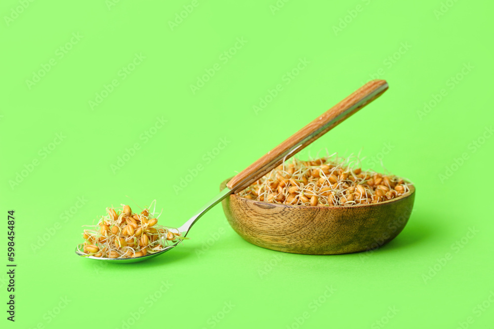 Bowl and spoon with sprouted wheat on light green background