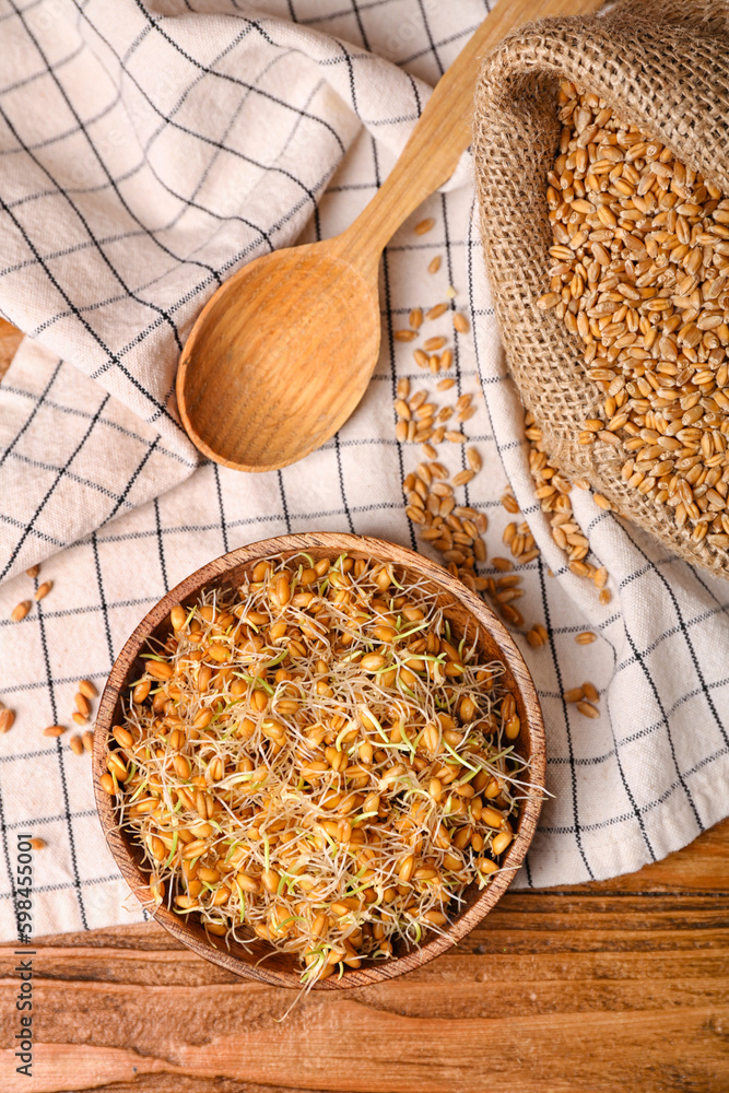 Bowl with sprouted wheat and spoon on wooden table