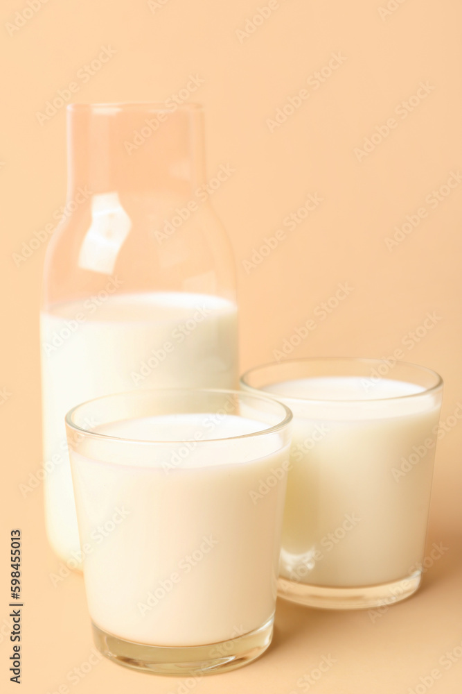 Bottle and glasses with milk on beige background