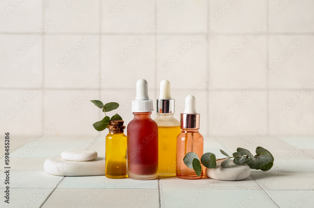 Composition with bottles of cosmetic oil, spa stones and eucalyptus branch on white tile