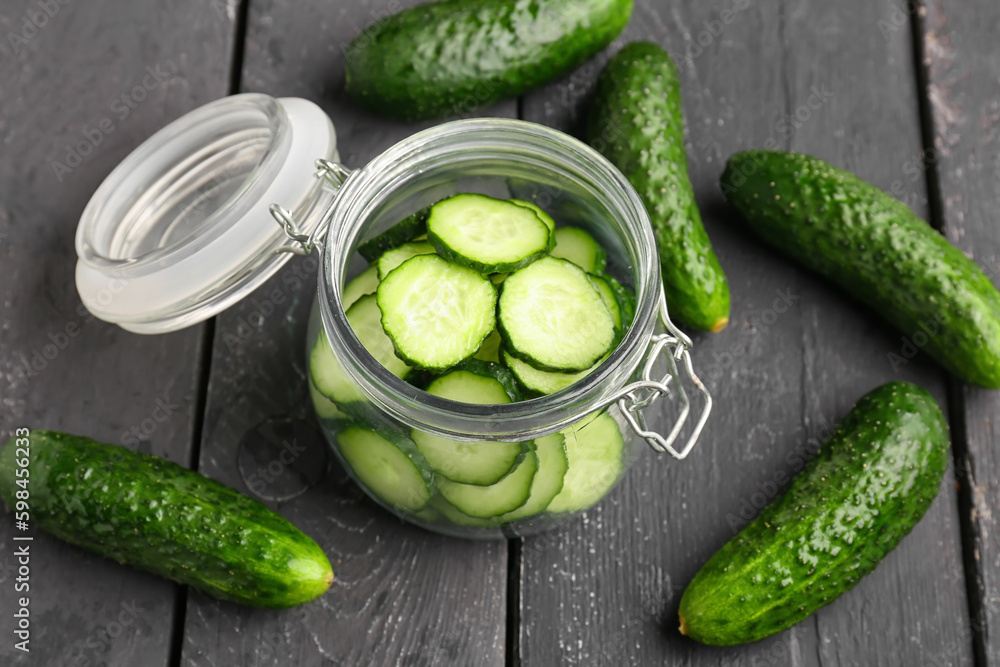 Jar with pieces of fresh cucumber on dark wooden background