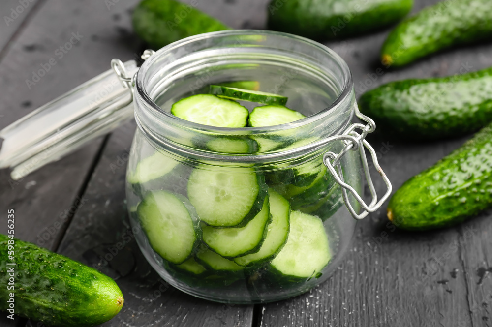 Jar with pieces of fresh cucumber on dark wooden background