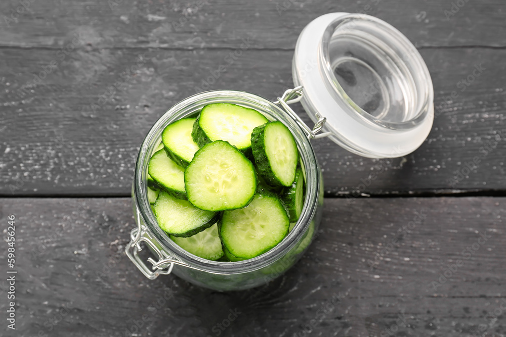 Jar with pieces of fresh cucumber on dark wooden background