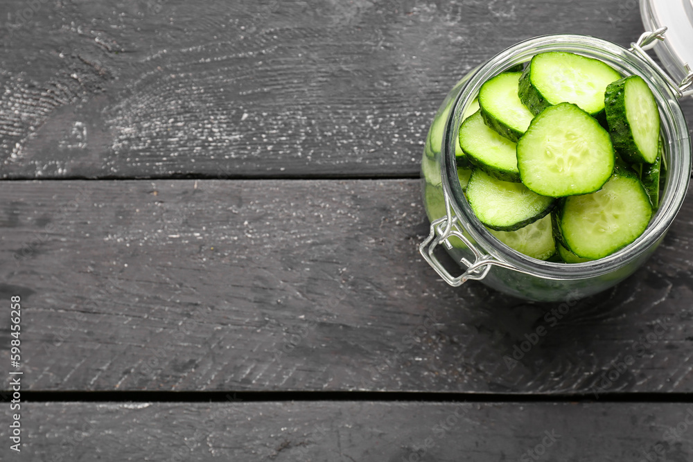 Jar with pieces of fresh cucumber on dark wooden background