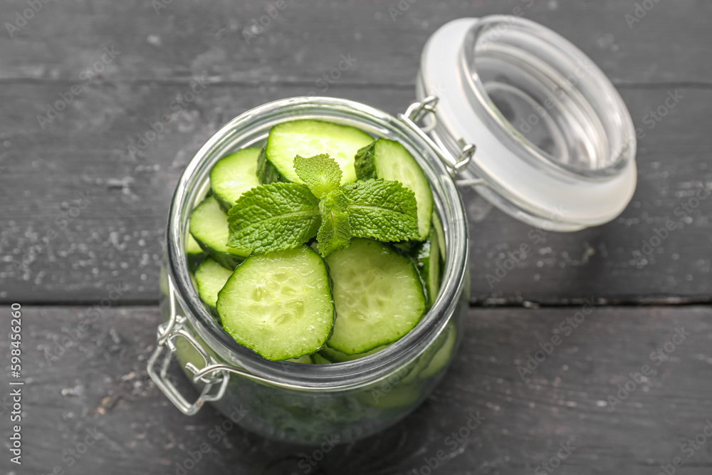 Jar with pieces of fresh cucumber on dark wooden background