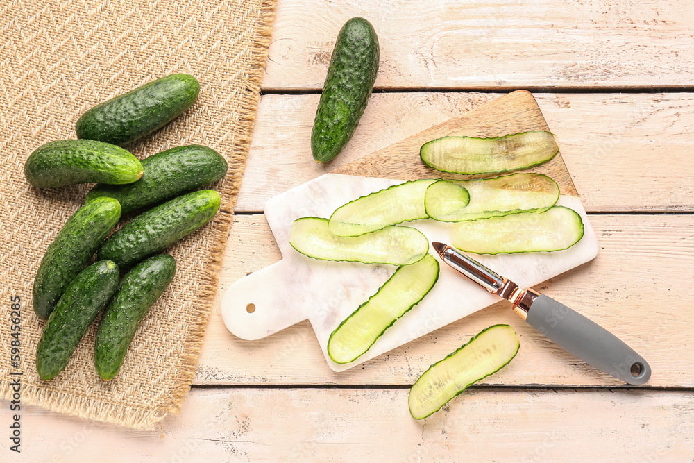 Board with fresh cut cucumbers on light wooden background