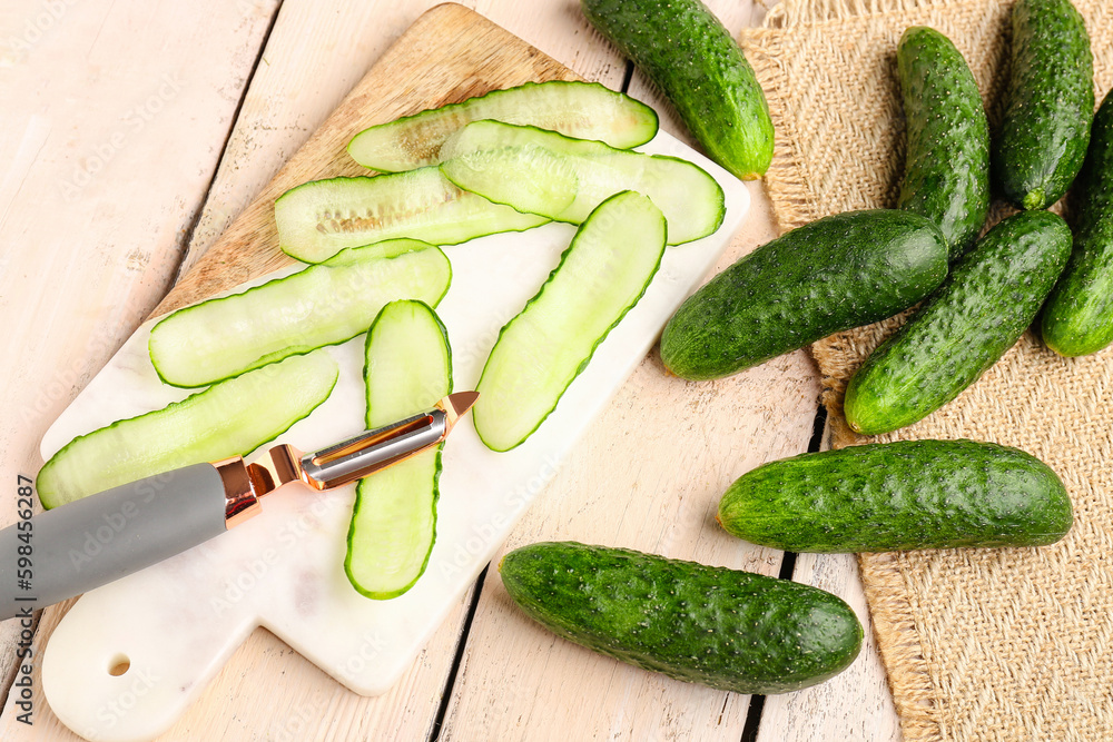 Board with fresh cut cucumbers on light wooden background