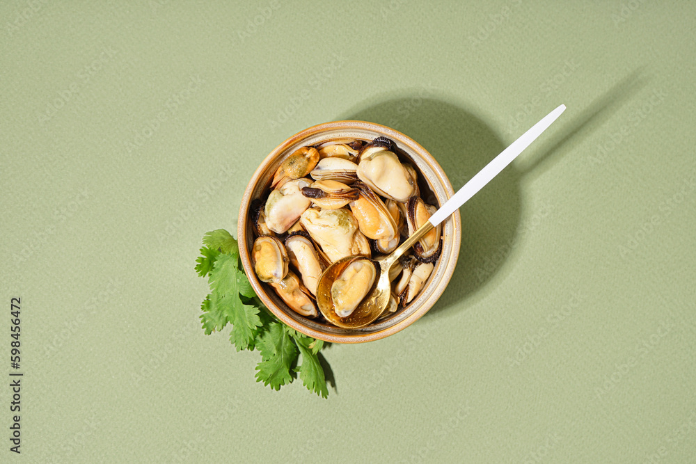 Bowl with pickled mussels on green background