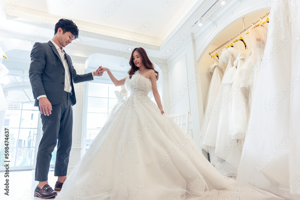 Asian beautiful bride trying on wedding gown with her fiance in studio. 