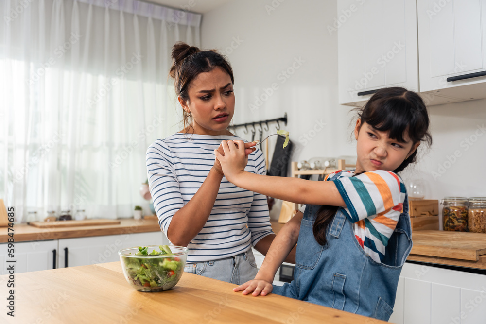 Caucasian mother teach and motivate young daughter eat green vegetable. 