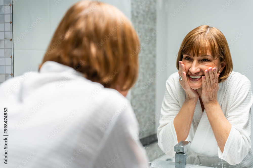 Caucasian senior woman wash and clean face with facial foam and water. 