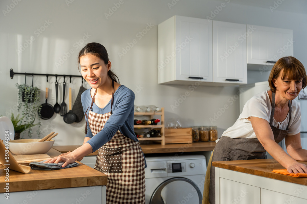 Caucasian senior elderly woman cleaning kitchen in house with daughter. 