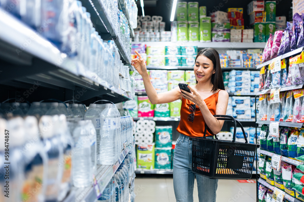 Asian young beautiful woman holding grocery basket walk in supermarket. 