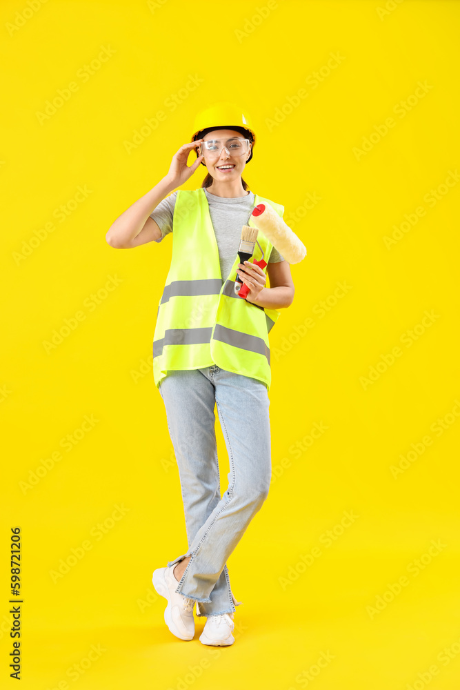 Female decorator with paint roller and brush on yellow background