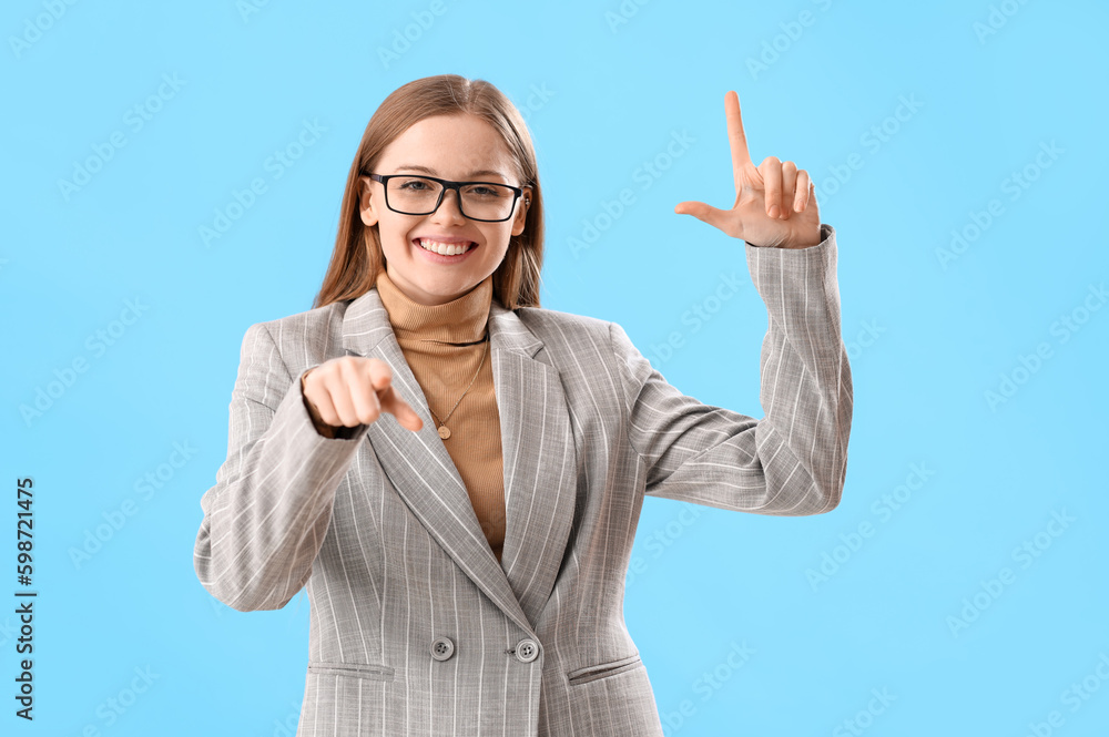 Young businesswoman showing loser gesture and pointing at viewer on blue background