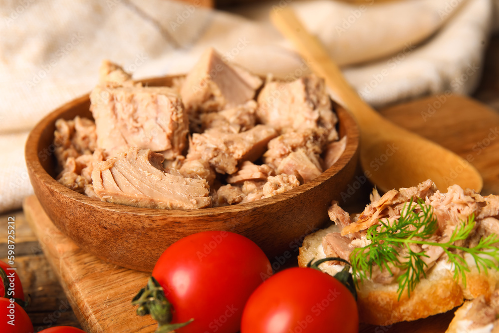 Bowl with delicious canned tuna and tomatoes on wooden board, closeup